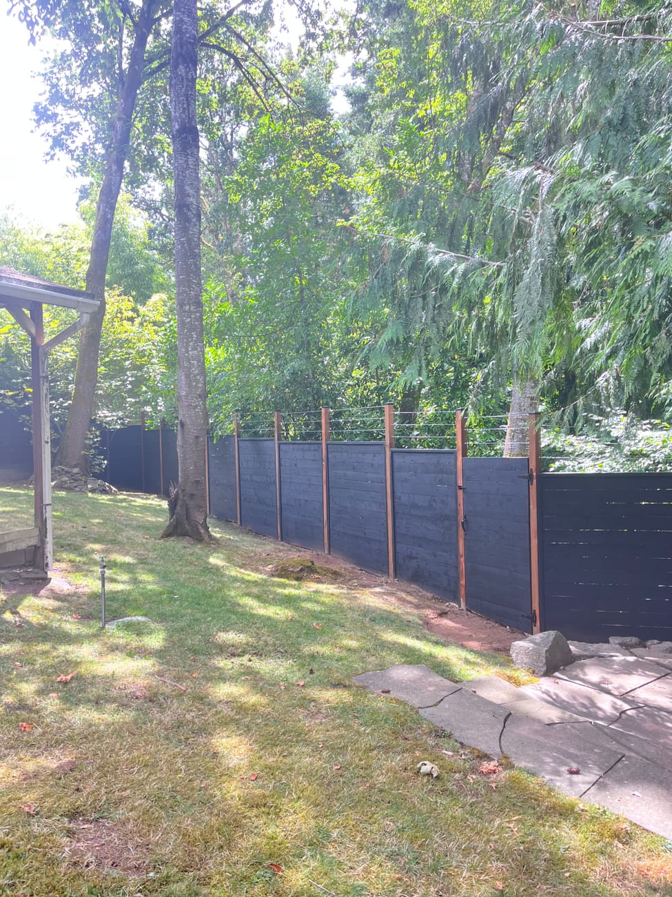 Long straight run of black horizontal-board fence disappearing into trees
