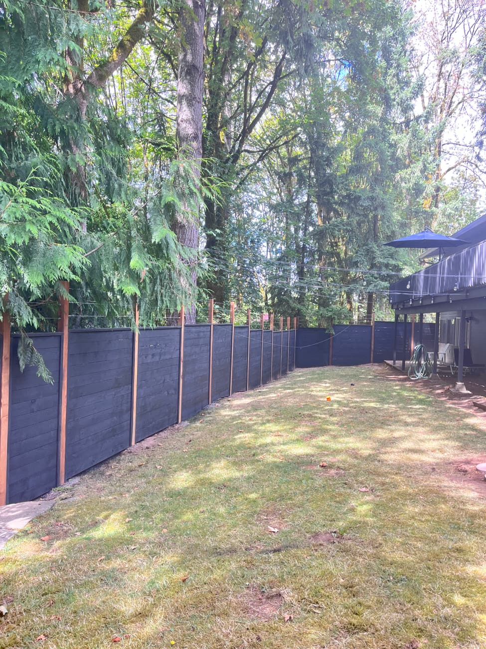 Black 8 ft privacy fence wrapping two sides of a wooded back yard