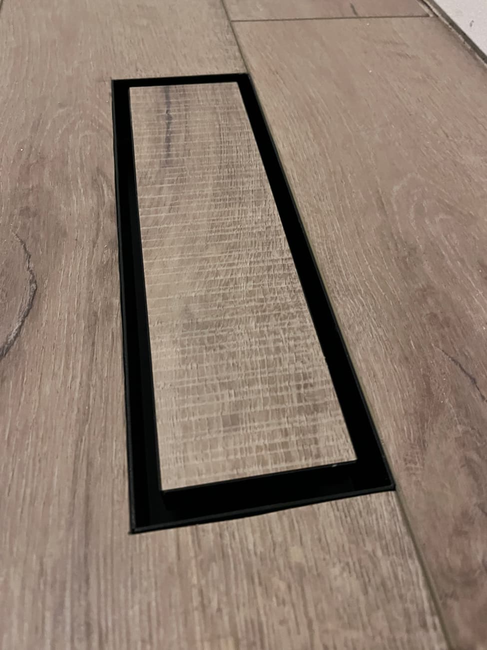 Floor register framed into the plank flooring with a black trim surround
