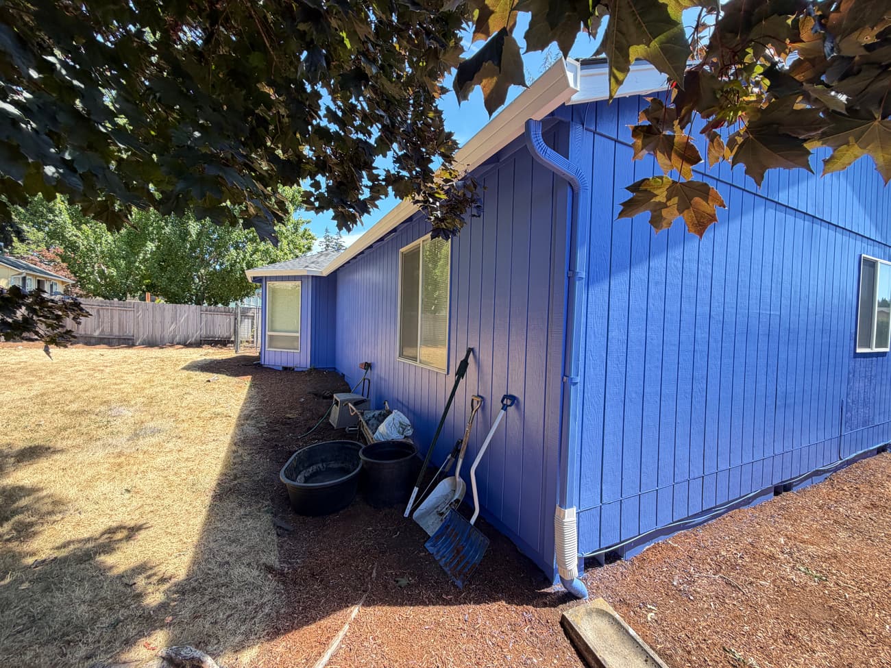 Long blue side elevation of the repainted house in full sun